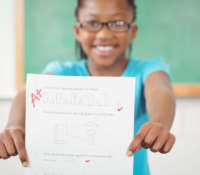 Portrait of proud pupil showing test result to camera in a classroom